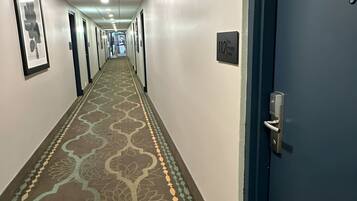 Un couloir d’hôtel avec un tapis à motifs, des portes et une porte bleue sur la droite.