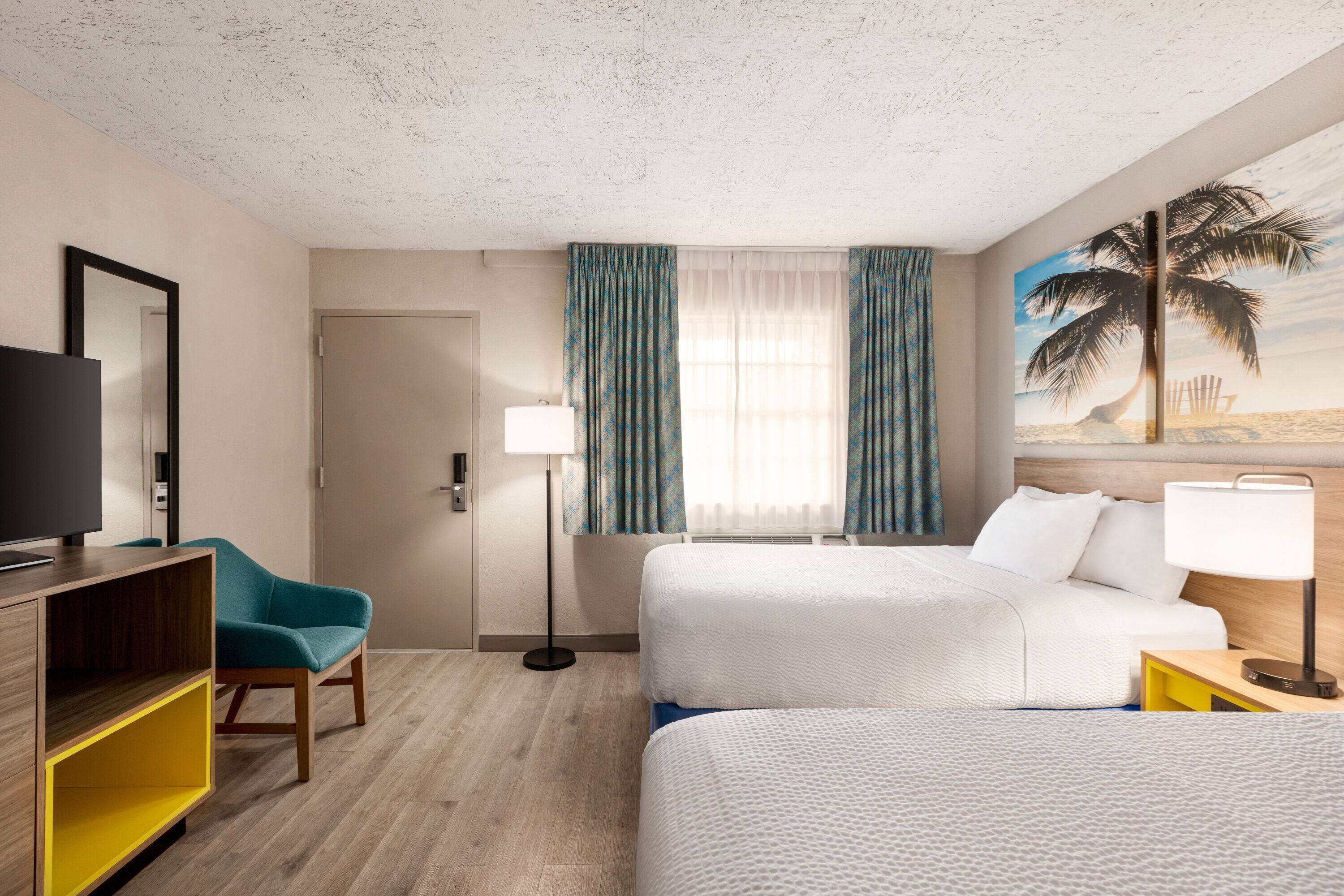 A hotel room with two beds, a TV, a desk, and a painting of a beach scene.