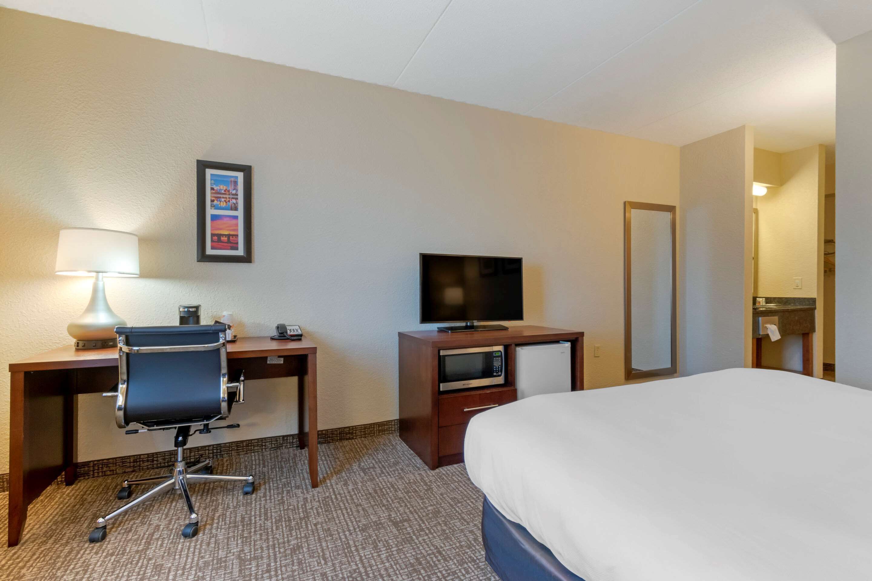 A hotel room with a bed, a desk with a lamp, a television, a microwave, and a mirror.
