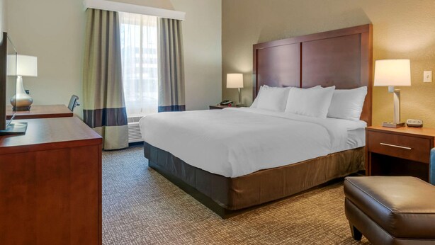 A hotel room with a large bed, a desk, a chair, and a window with curtains.