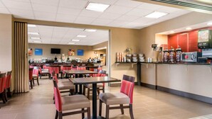 A spacious dining area with multiple tables and chairs, a self-service beverage station, and a kitchen in the background.
