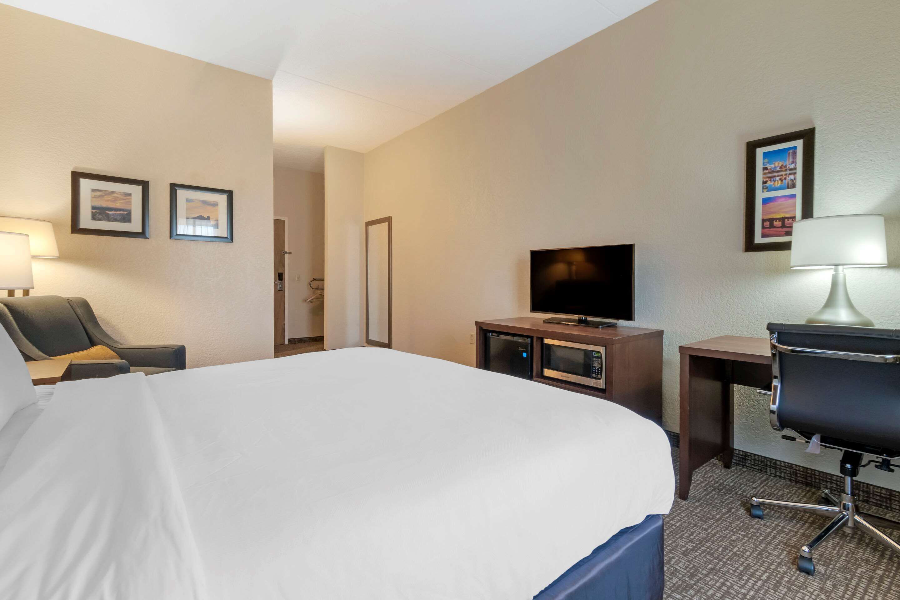 A hotel room with a large bed, a desk with a chair, a television, and a microwave.