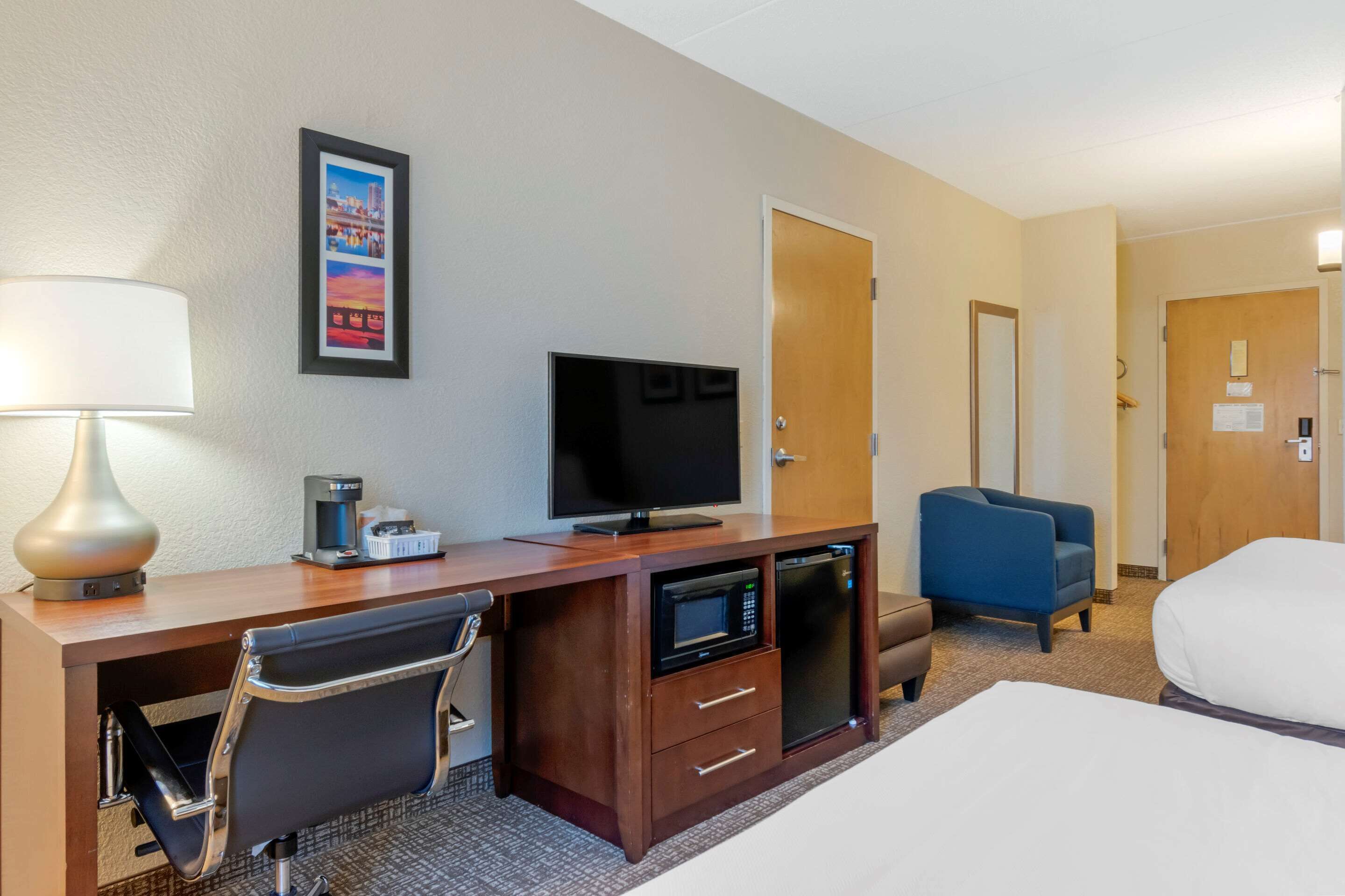 Habitación de hotel con escritorio, televisión, microondas y una silla.