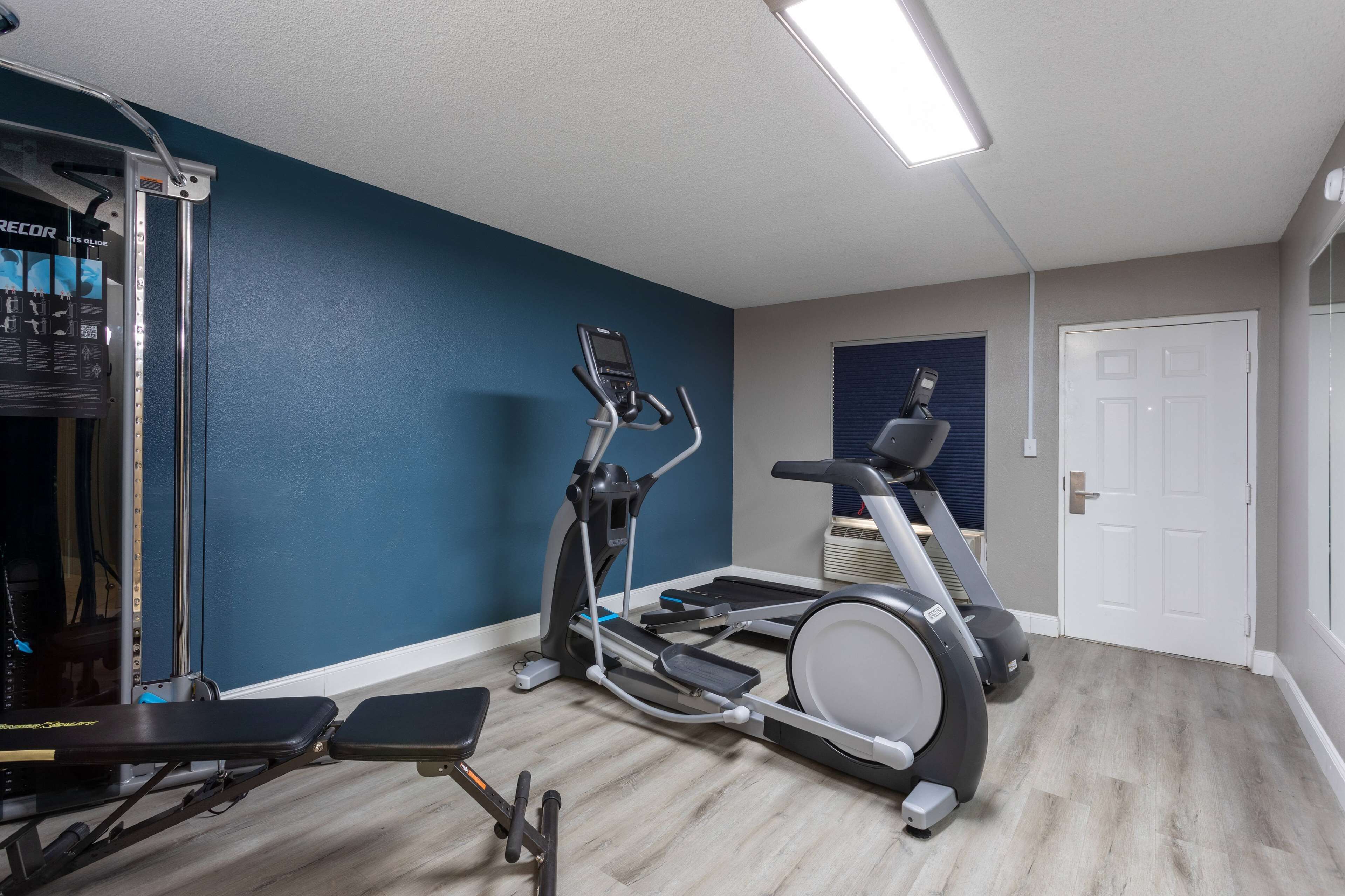 A home gym with a treadmill, elliptical, and weight bench.