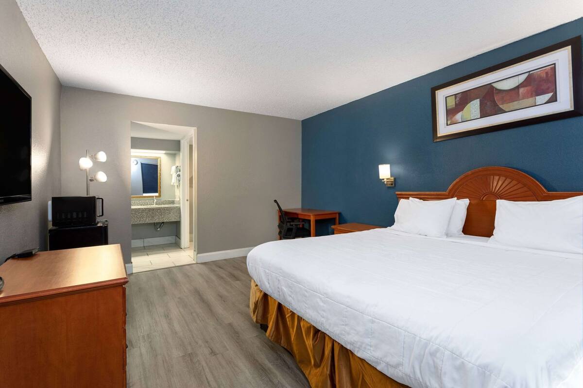 Une chambre d’hôtel avec un lit, un bureau, une télévision, une salle de bain et un tableau au mur.