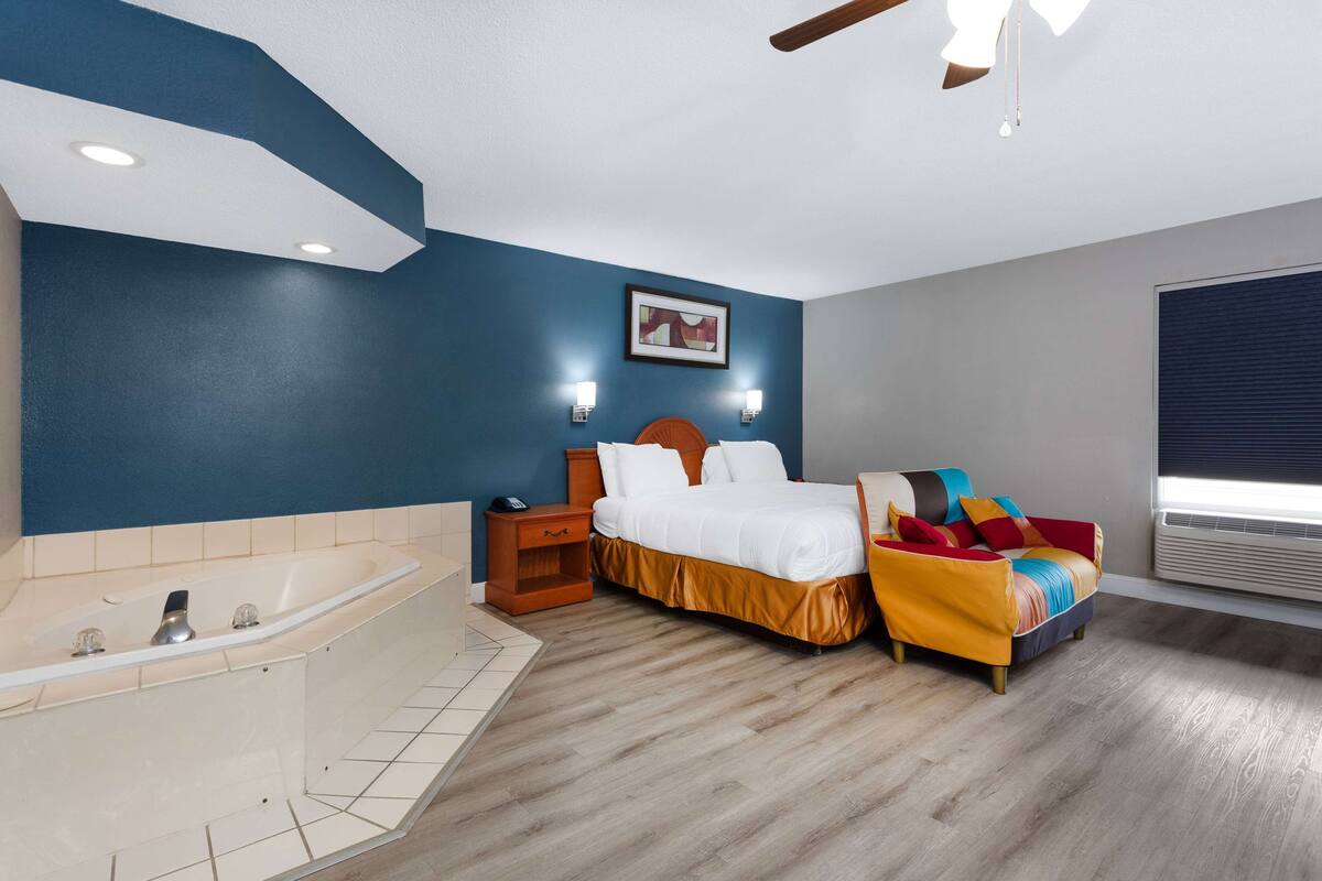 Une chambre avec une grande baignoire, un lit avec une literie aux couleurs vives et un ventilateur de plafond.