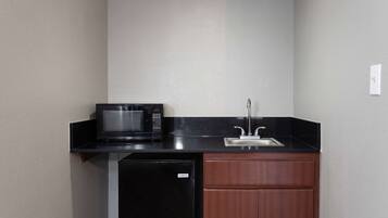 Una kitchenette compacta con un microondas negro, un lavamanos y un refrigerador pequeño.