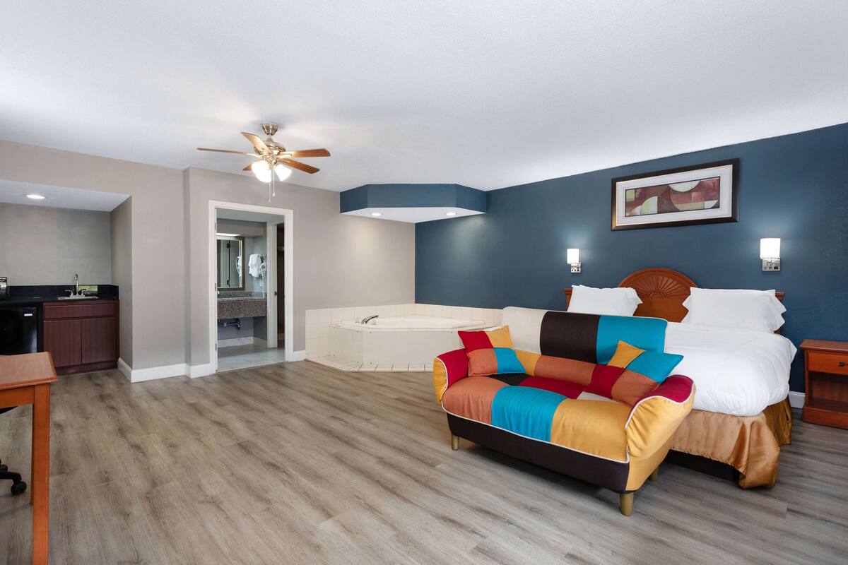 Une chambre avec un lit, un ventilateur de plafond, une baignoire et un coin cuisine.