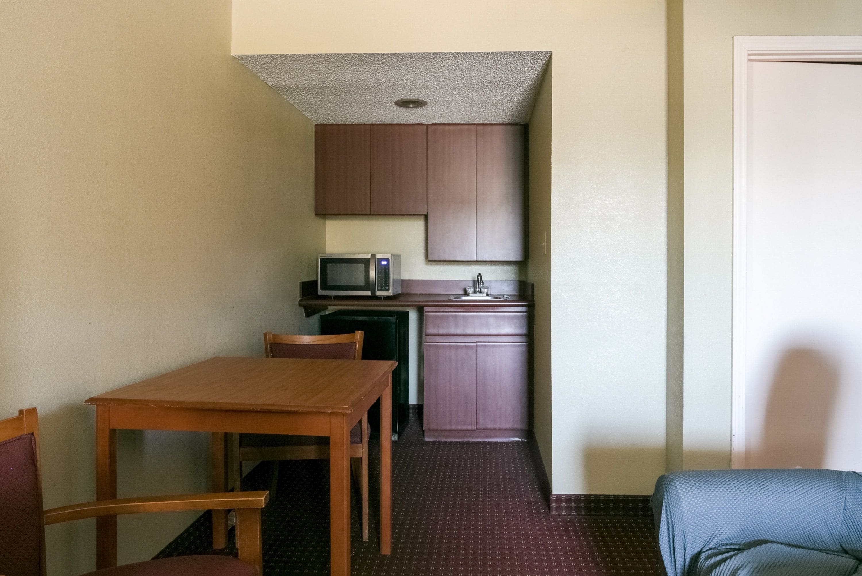 A compact kitchen with a microwave, sink, and cabinets. There is a wooden table and two chairs in the dining area.