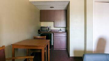 A compact kitchen with a microwave, sink, and cabinets. There is a wooden table and two chairs in the dining area.