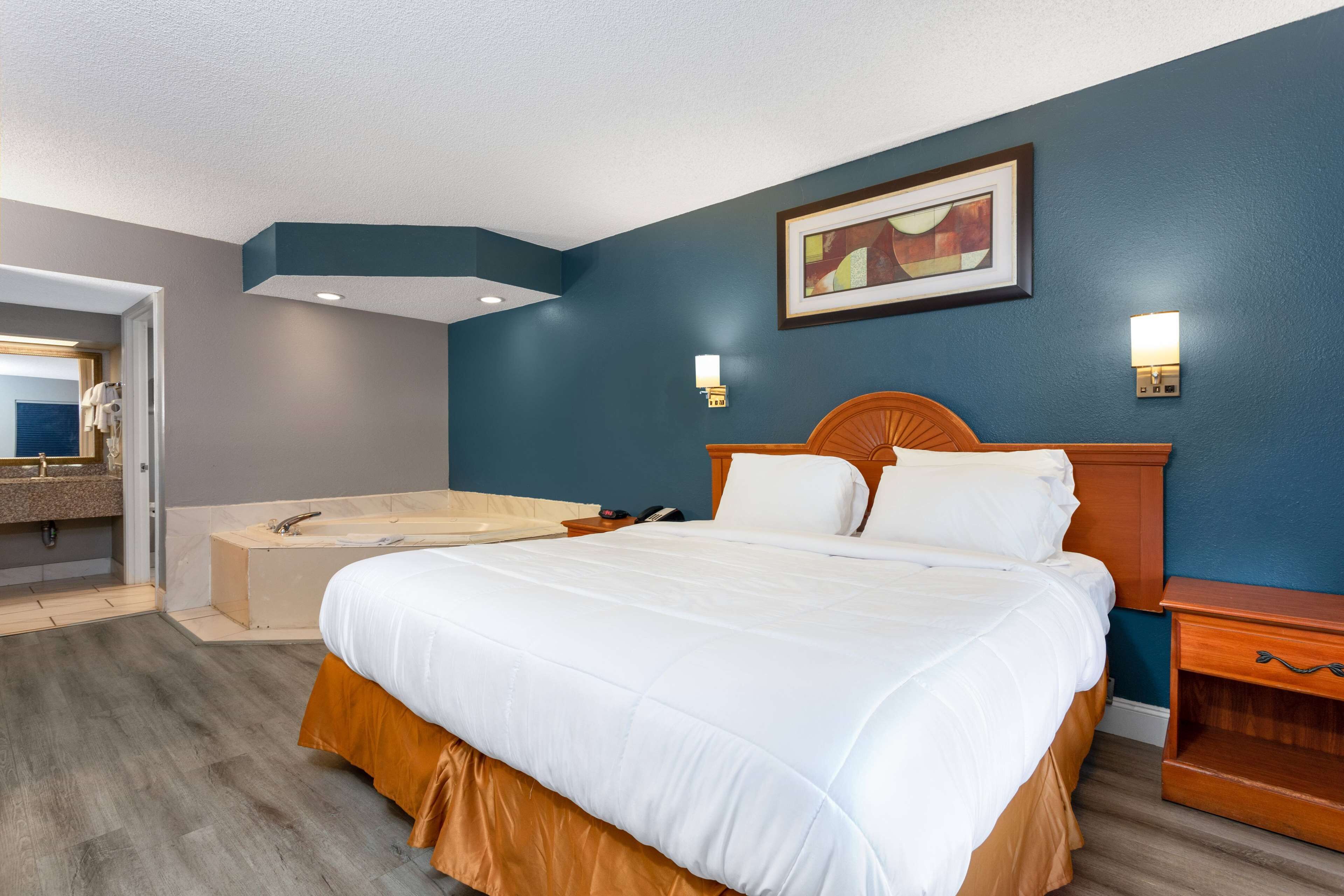 A hotel room with a large bed, a wooden headboard, a bathtub, and a painting on the wall.
