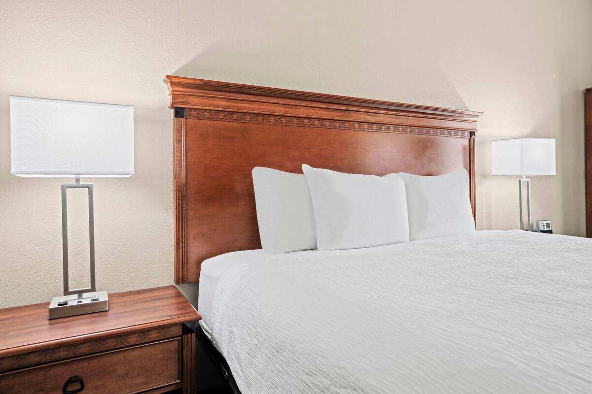 Una habitación de hotel con cabecera de madera, cubrecama blanco y dos lámparas de noche.