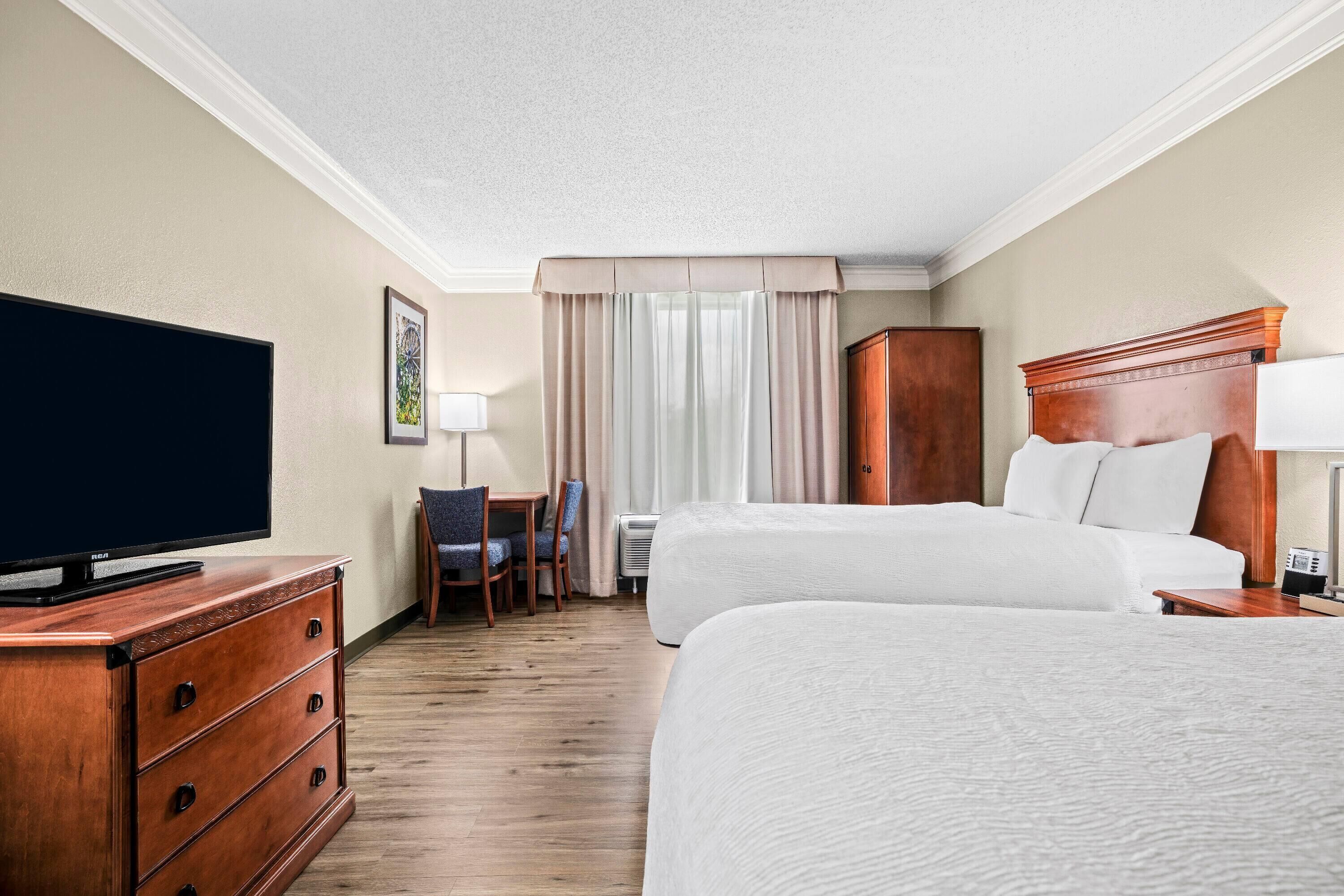 Een hotelkamer met een groot bed, een televisie op een houten dressoir, een bureau met een stoel en een raam met gordijnen.