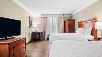 Een hotelkamer met een groot bed, een televisie op een houten dressoir, een bureau met een stoel en een raam met gordijnen.
