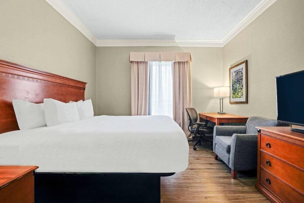 Habitación de hotel con una cama grande, un escritorio, una silla, un televisor y un aparador.