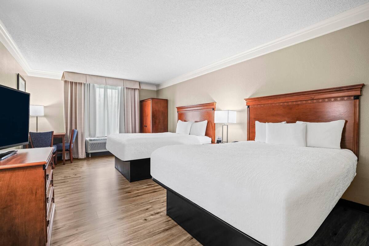 Habitación de hotel con dos camas, un escritorio, un televisor y una silla.
