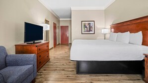 Habitación de hotel con cama, televisor sobre una cómoda de madera, una silla y un pasillo que conduce a otra habitación.