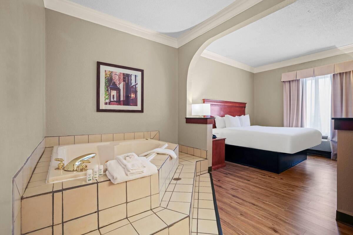 Habitación de hotel con una cama grande, baño privado con bañera y un cuadro en la pared.