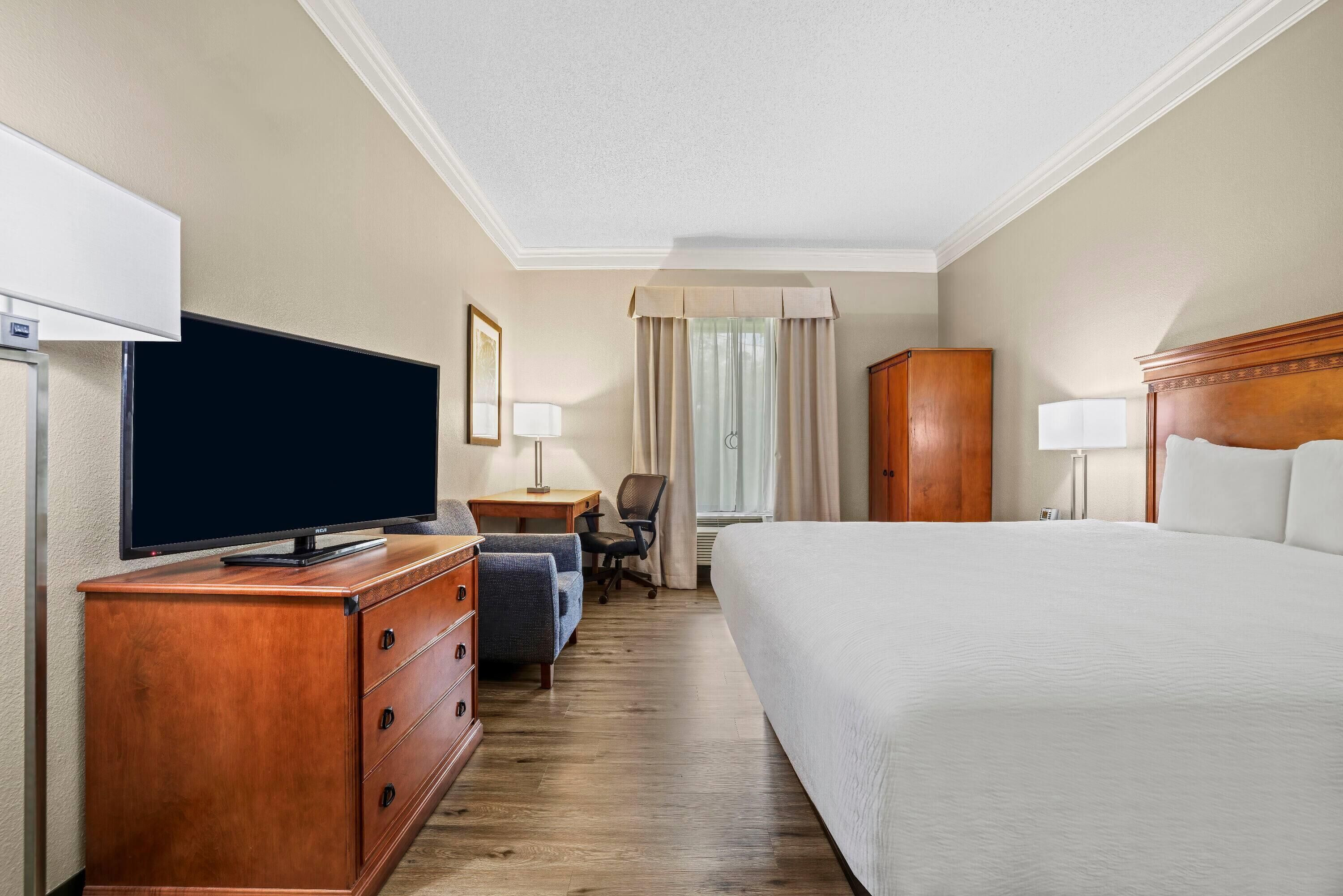 Habitación de hotel con una cama grande, un televisor de pantalla plana sobre un aparador de madera, un escritorio con lámpara y una silla.