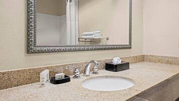 A bathroom with a large mirror, a sink, and a shower.