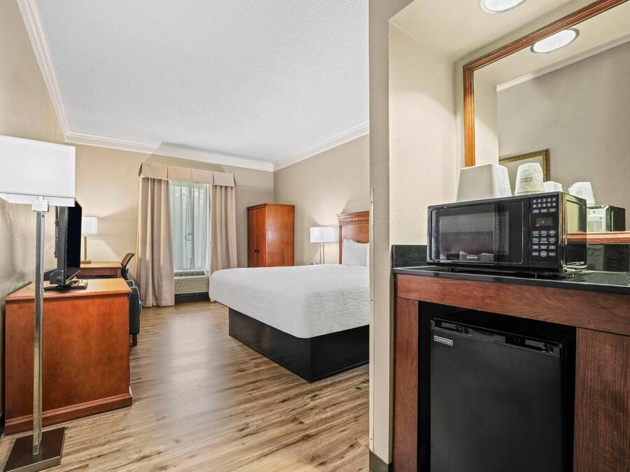 Habitación de hotel con un escritorio de madera, una cama, microondas y un refrigerador pequeño.