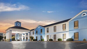Un hotel con fachada azul y blanca, vestíbulo cubierto y estacionamiento.