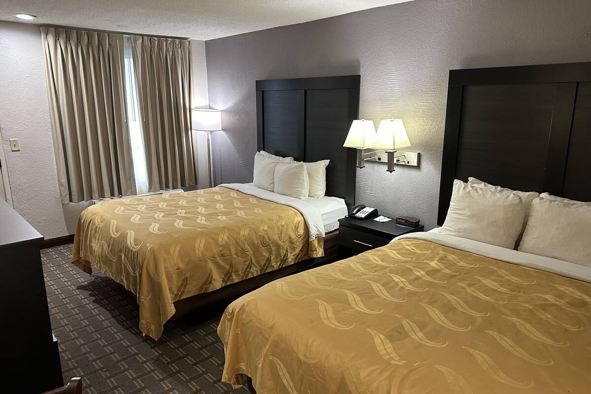 A hotel room with two beds, a desk, and a lamp.