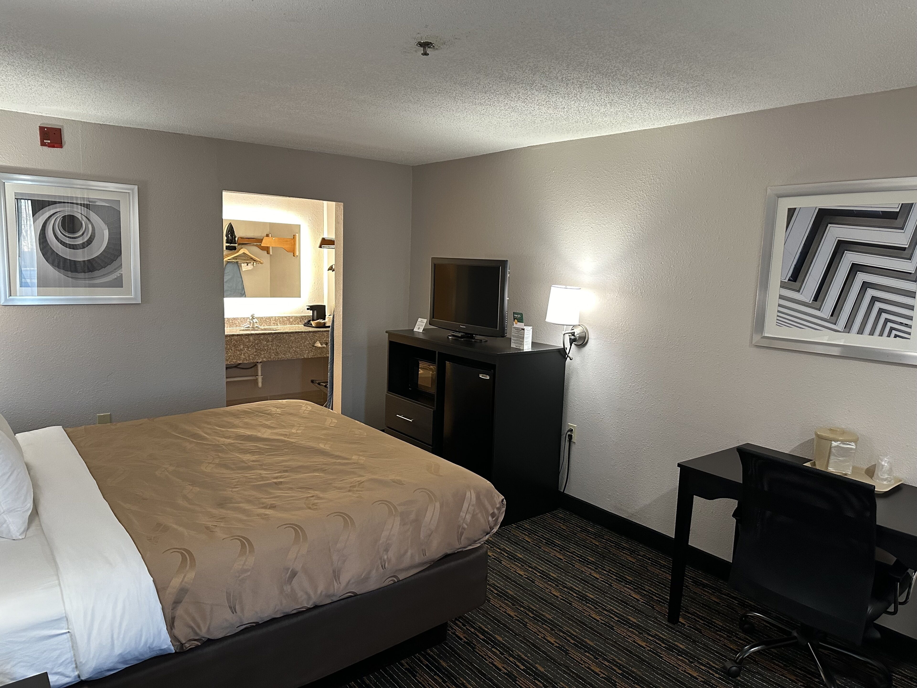 Una habitación de hotel con cama, escritorio, televisor y espejo.