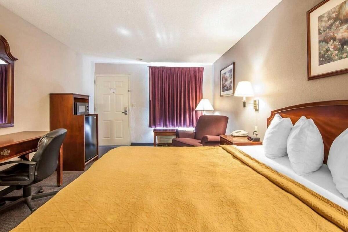 A hotel room with a bed, desk, chair, and a door.