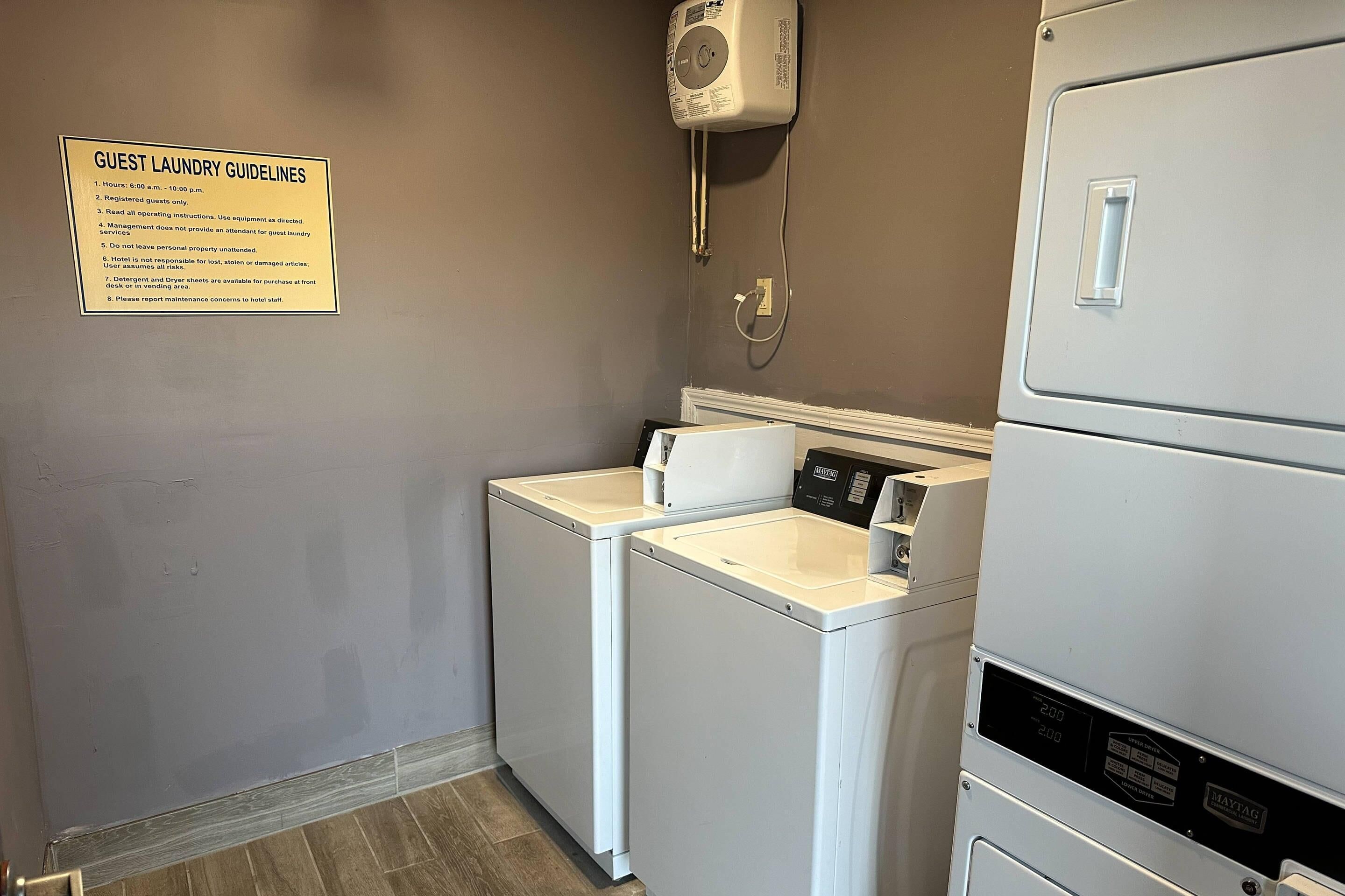 A laundry room with a sign detailing guest laundry guidelines, a washing machine, a dryer, and a wall-mounted dryer.