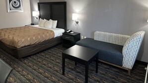A hotel room with a bed, bedside table, chair, and a small table.