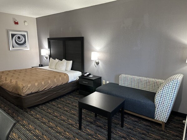 Ein Hotelzimmer mit Bett, Nachttisch, Stuhl und kleinem Tisch.
