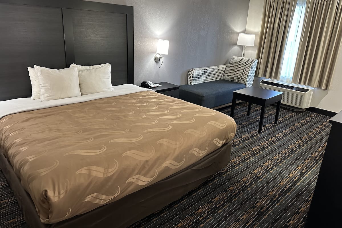 A hotel room with a large bed, a desk, a chair, and a window with curtains.