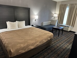 A hotel room with a large bed, a desk, a chair, and a window with curtains.
