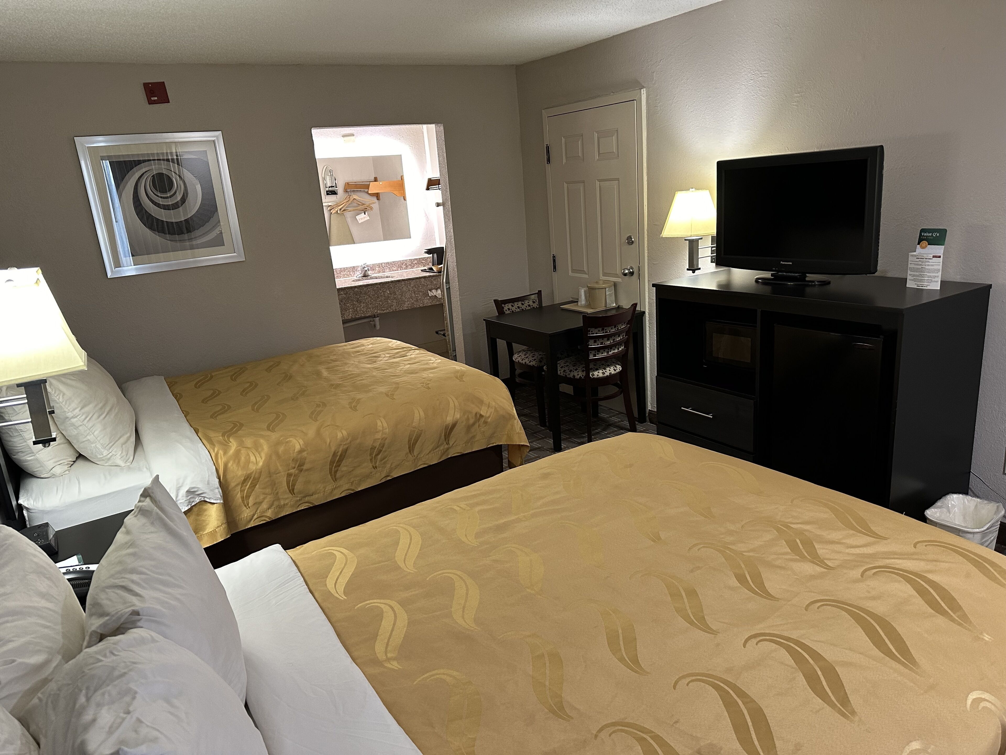 Una habitación de hotel con dos camas, un escritorio, un televisor y un espejo.