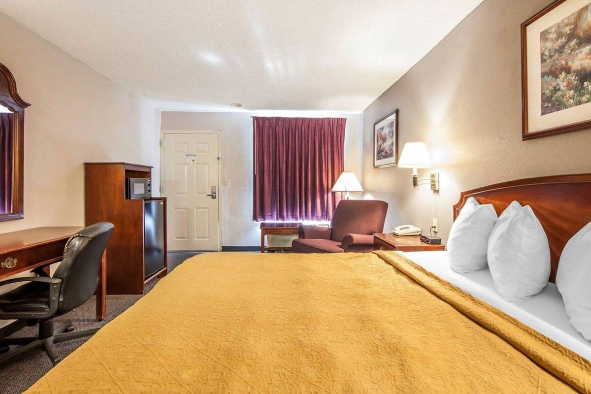 A hotel room with a bed, desk, chair, and a door.
