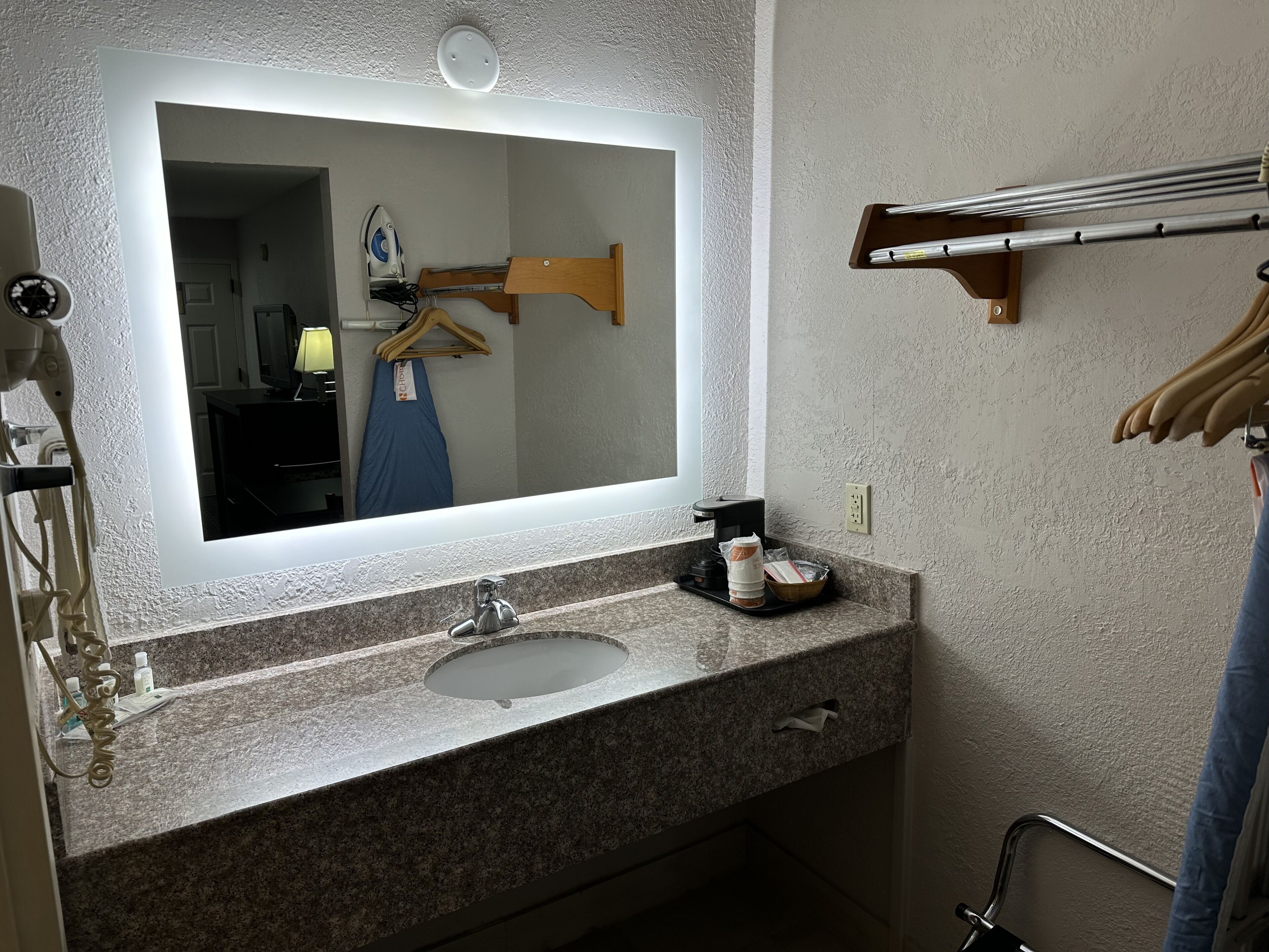 Un baño con encimera de granito, un lavabo, un espejo, un perchero y una zona de ducha.