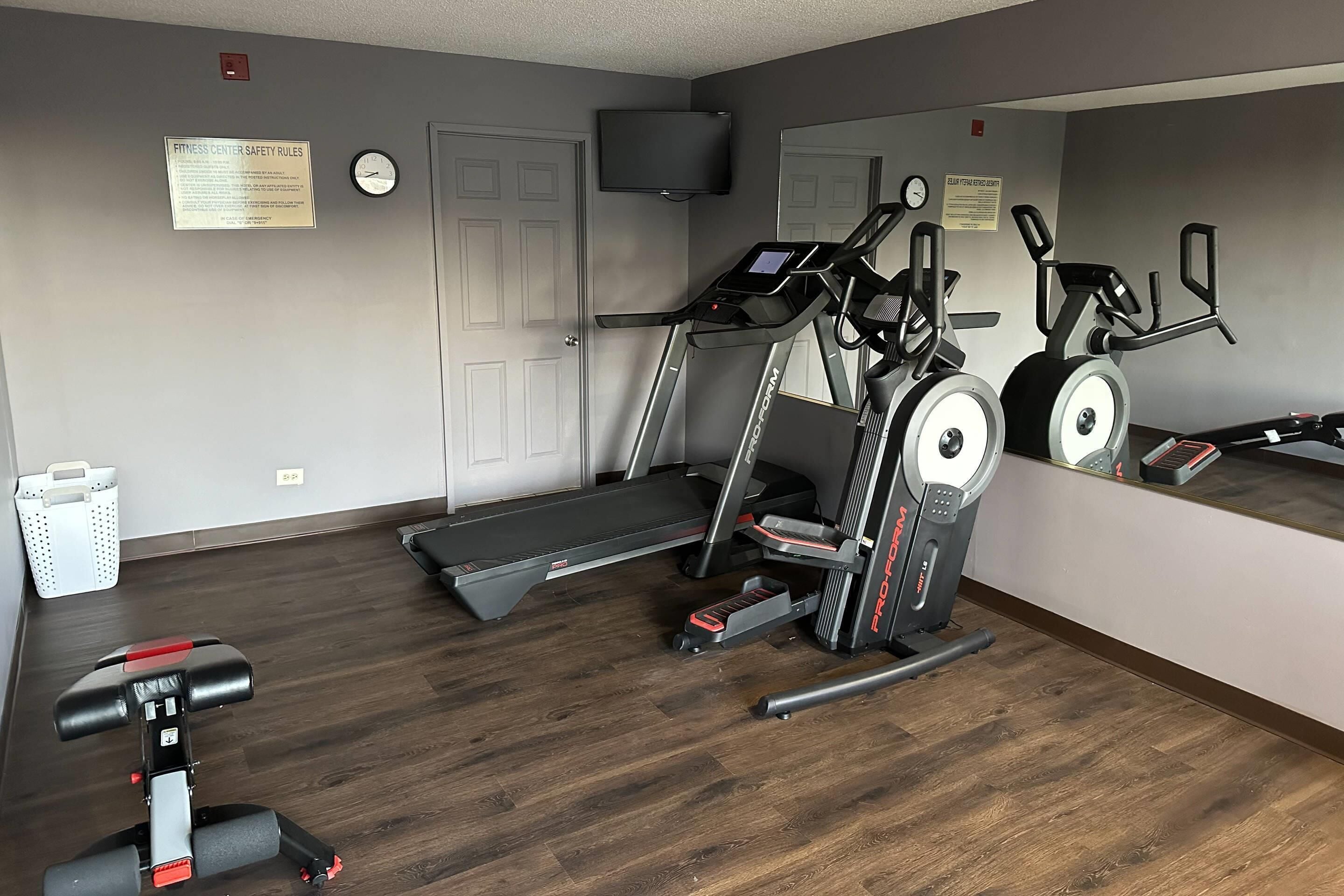 Un gimnasio con cintas de correr, elípticas y un espejo grande.