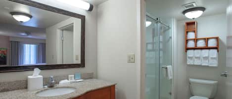 A hotel bathroom with a granite countertop sink, a mirror, a glass shower enclosure, and a toilet.