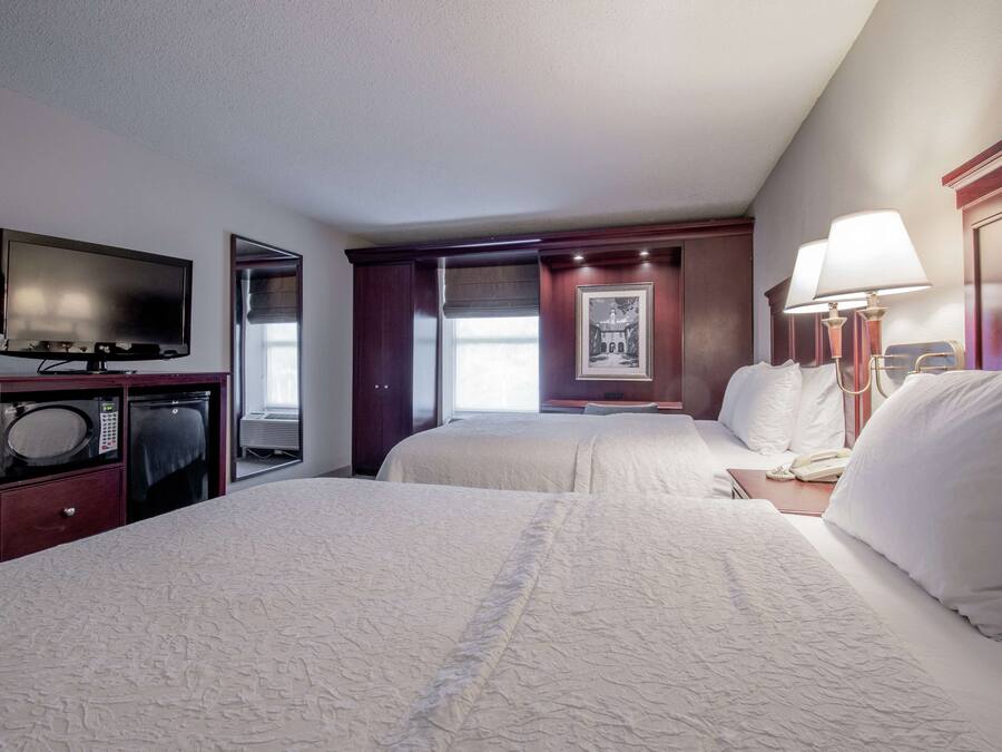 A hotel room with two beds, a TV, a desk, and a window with a view.