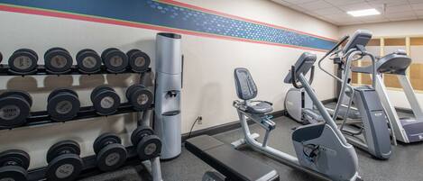 Une salle de sport équipée de matériel d’exercice, notamment des haltères, un banc et des appareils de cardio.