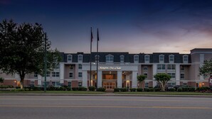 Ein Hampton Inn & Suites Hotel mit einer symmetrischen Fassade, zahlreichen Fenstern und einer Fahnenstange mit Flaggen.