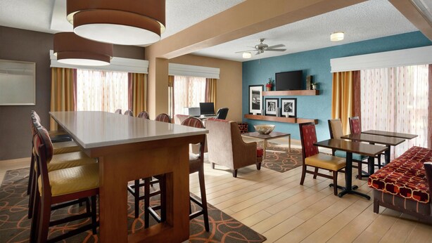 A hotel room with a dining area, a TV mounted on the wall, and a ceiling fan.