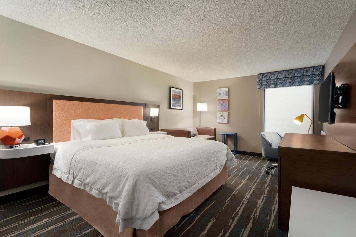 A hotel room with a bed, bedside tables, a desk, a chair, and a television.