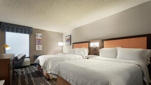A hotel room with two beds, a desk, a chair, a lamp, and artwork on the walls.
