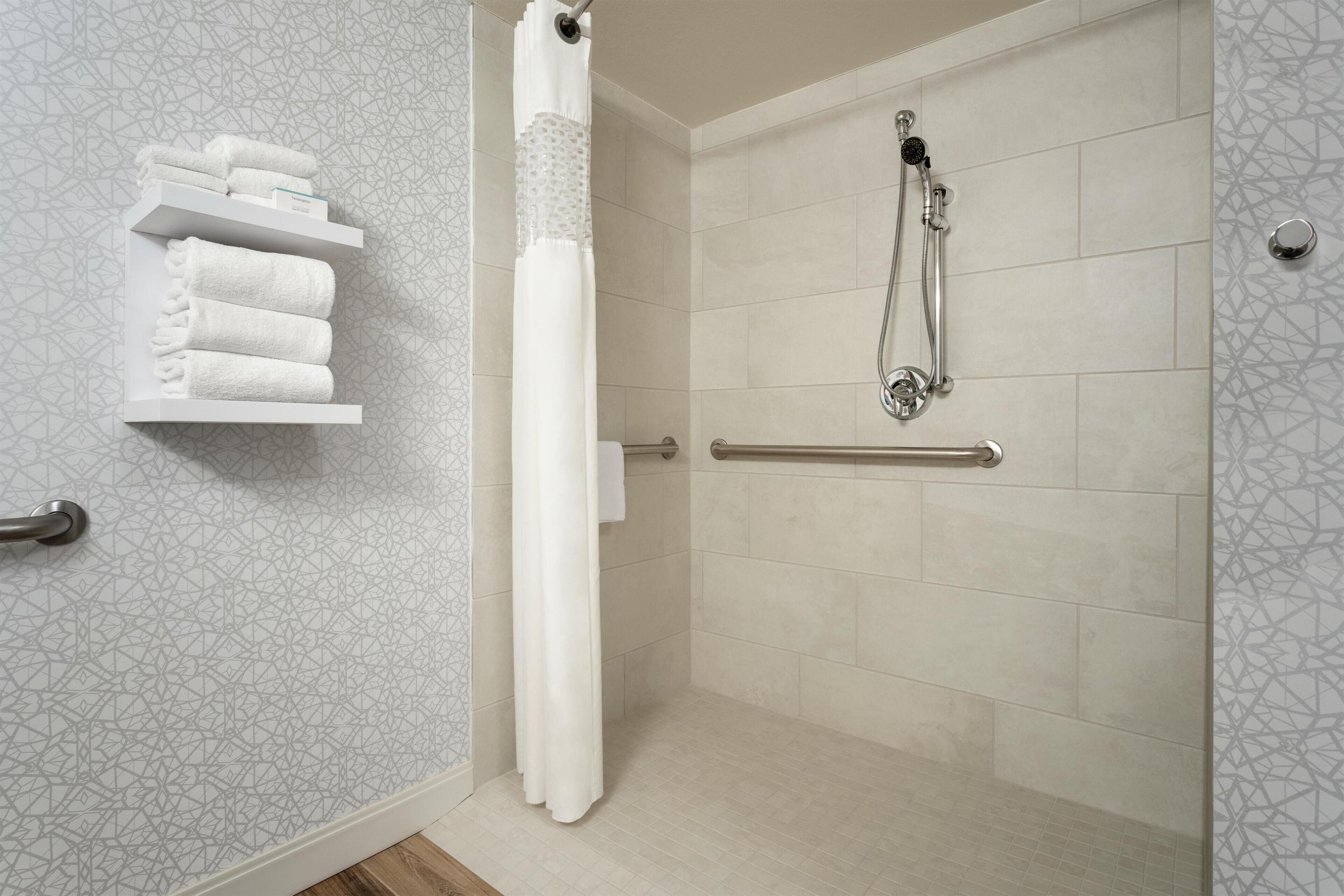 A shower area with a handrail, a towel rack with folded towels, and a showerhead.