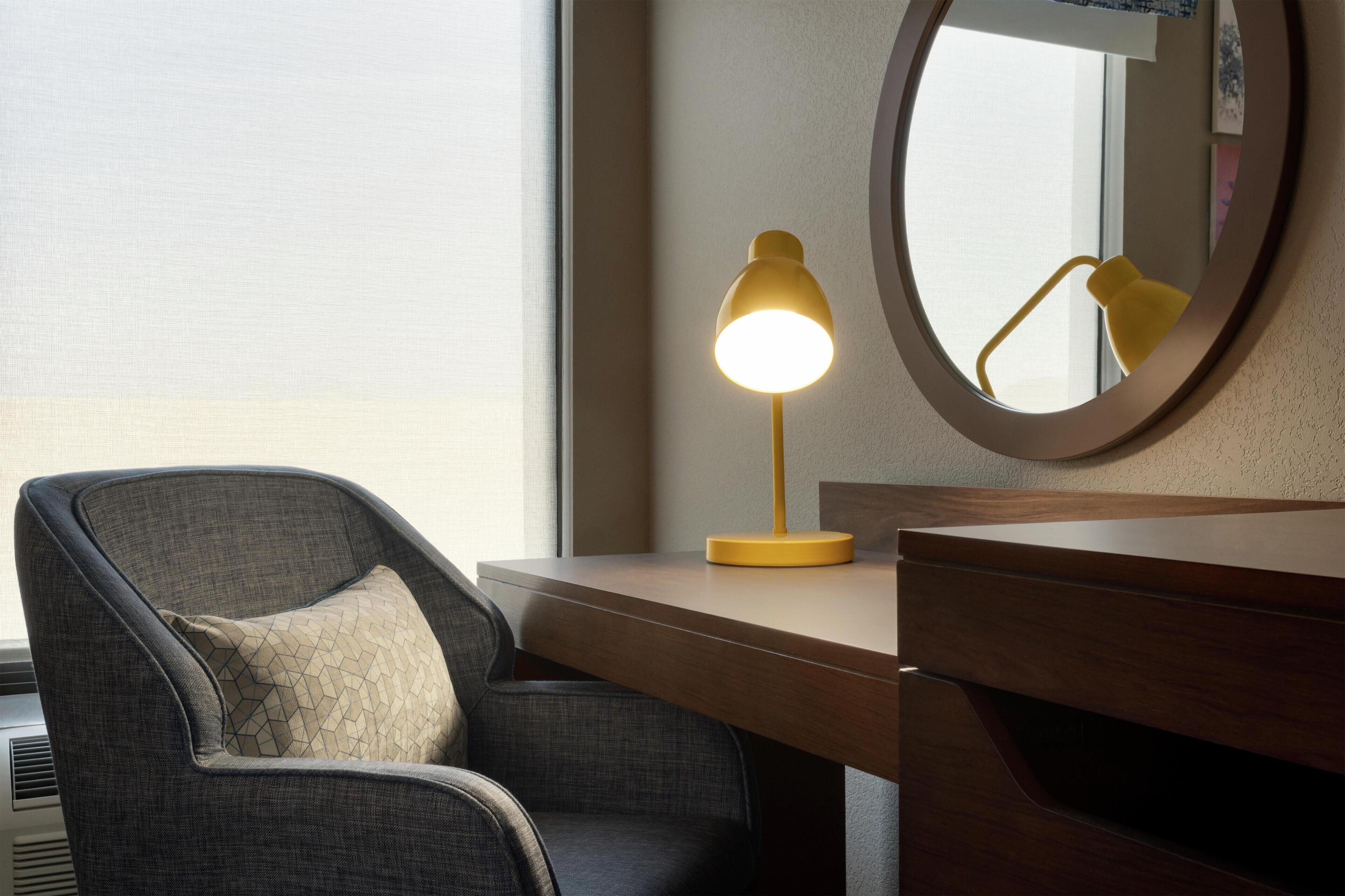 Una habitación moderna con escritorio, silla y espejo redondo.
