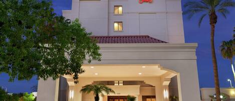 A hotel with a prominent sign, a covered entrance, and a palm tree in the foreground.