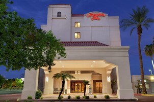 Un hotel con un letrero llamativo, un acceso cubierto y una palmera en primer plano.