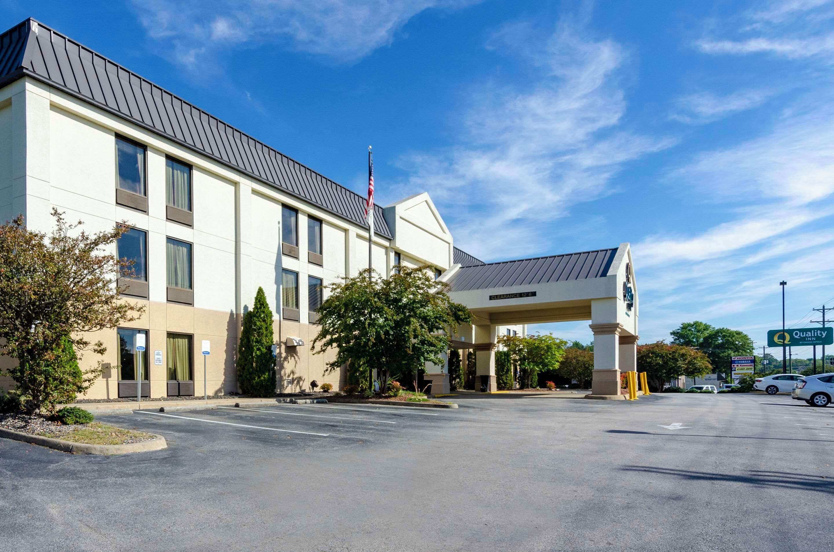 A modern hotel with a covered entrance, a parking lot, and a clear blue sky.